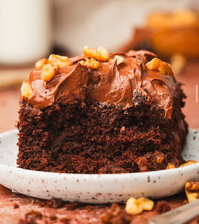 Slice of chocolate cake with frosting and walnuts on white plate