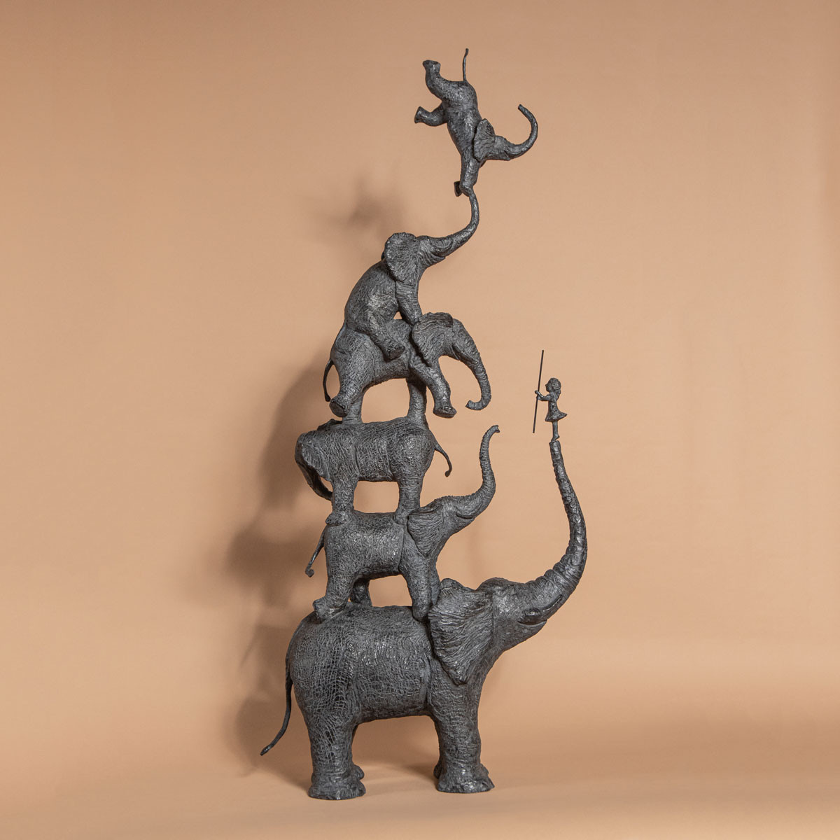 Sculpture of stacked elephants with a monkey on top against a beige background