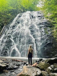Woman standing on rocks viewing a large cascading waterfall surrounded by green trees
