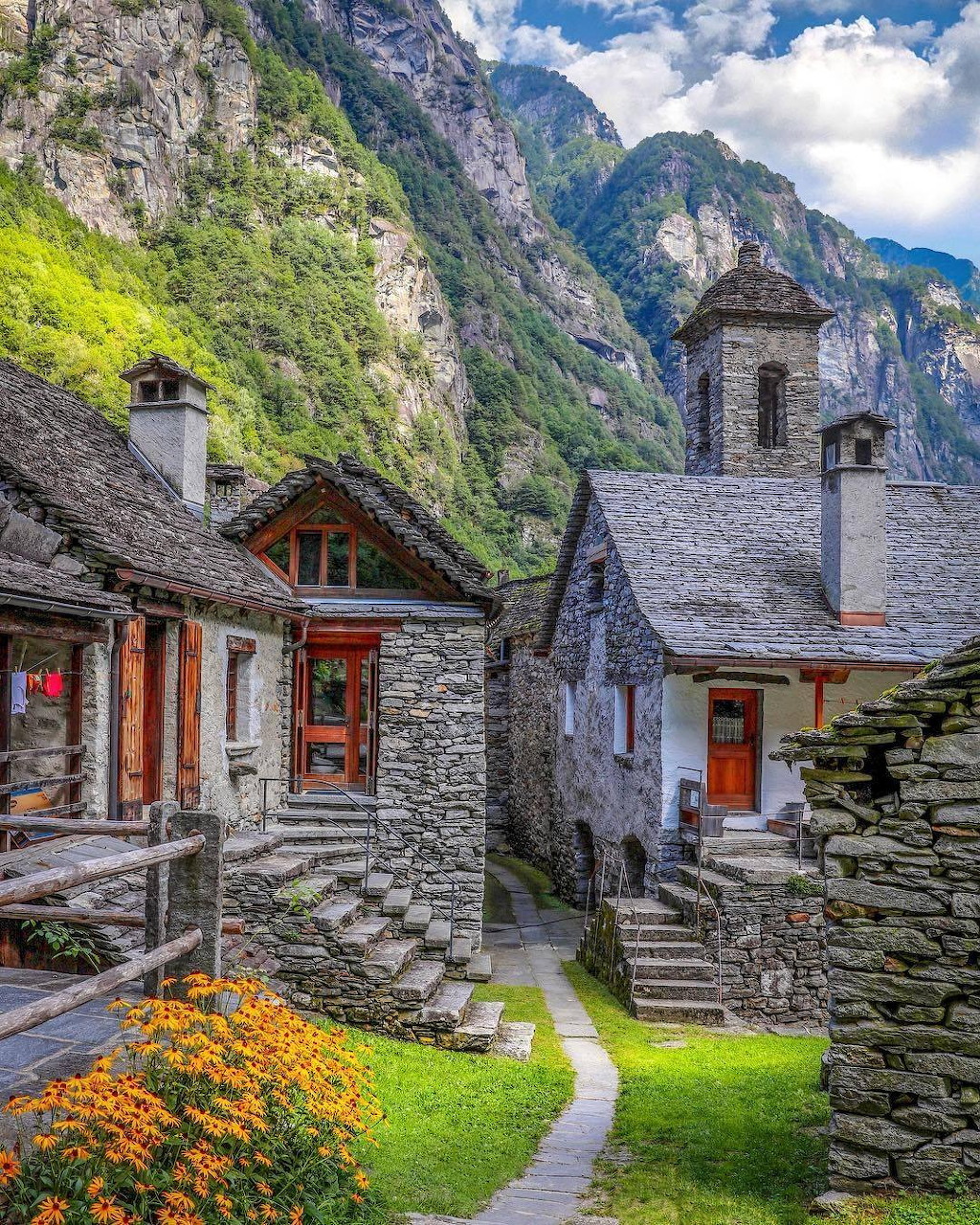 Traditional stone houses with church bell tower in alpine village beneath towering mountain cliffs