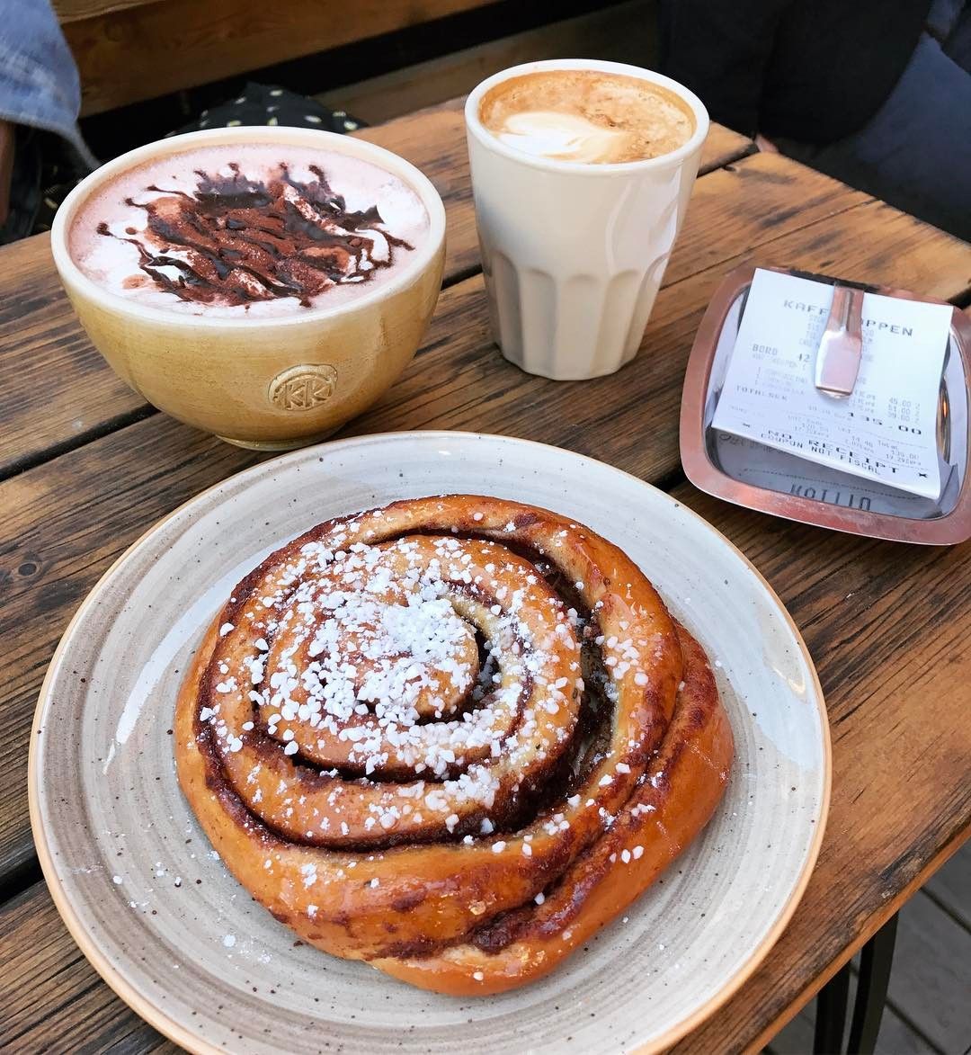 Cinnamon roll on a plate with two cups of coffee on a wooden café table
