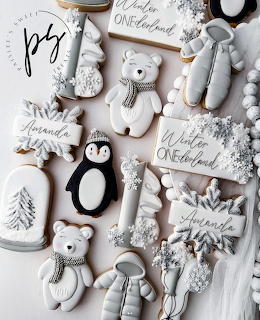 Festive white and gray frosted cookies shaped like polar bears, penguins, and Christmas trees on a light background