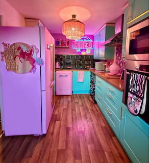 Colorful retro kitchen with teal cabinets, pink neon glow, white fridge, and vintage decor