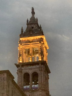 Illuminated baroque church bell tower with arched openings and ornate crown against evening sky
