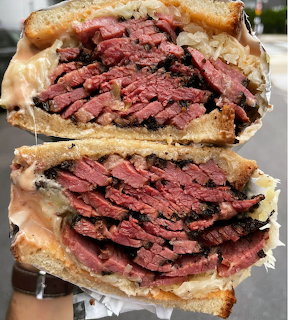 Two halves of a pastrami sandwich stacked, showing thick layers of sliced meat on toasted bread