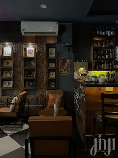 Dimly lit cafe interior with leather couch, framed pictures on brick wall, and bar area with bottles
