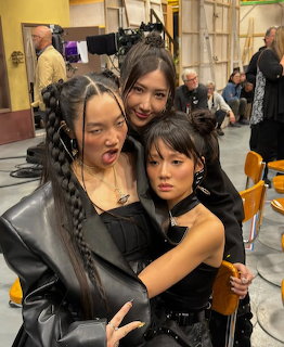 Three women in black leather outfits posing together in an indoor studio setting