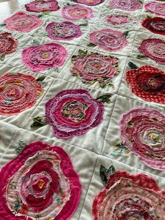 Handmade quilt with circular fabric rose appliqués in pink and red on cream background