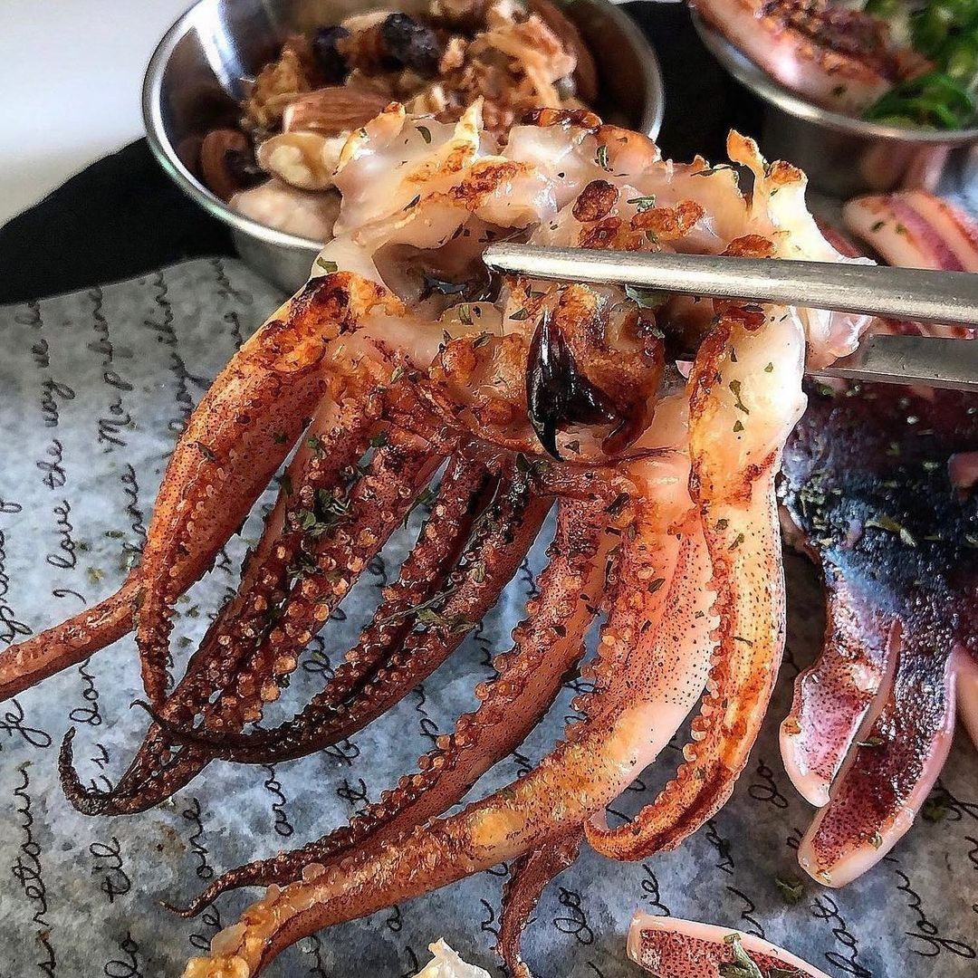 Close-up of grilled squid with charred tentacles held by chopsticks over a plate
