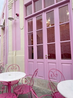 Pink café exterior with pink doors, pink metal chairs, and white tables on a patio