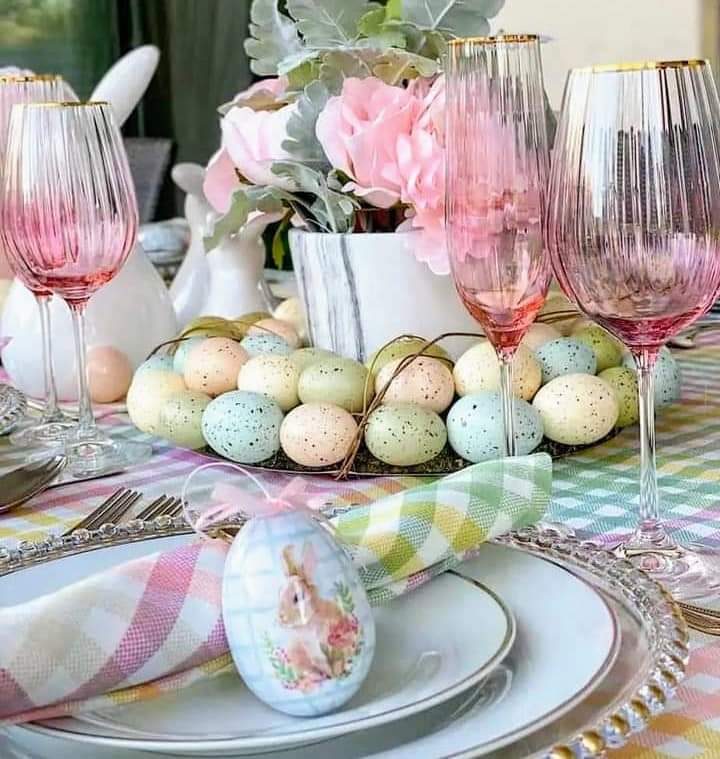 Easter dining table with colorful decorated eggs, pink glassware, flowers, and pastel place settings