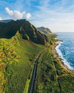 Aerial photo of a road winding along green coastal mountains beside the blue ocean