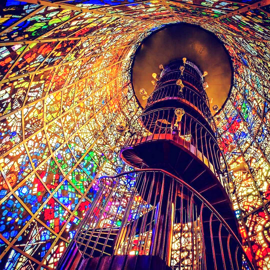 Looking up at a spiral tower staircase surrounded by colorful mosaic stained glass
