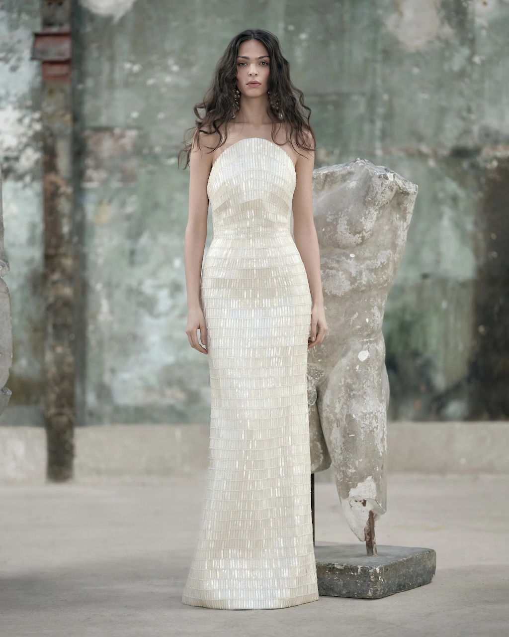 Woman in white sequined wedding dress standing on runway with weathered background