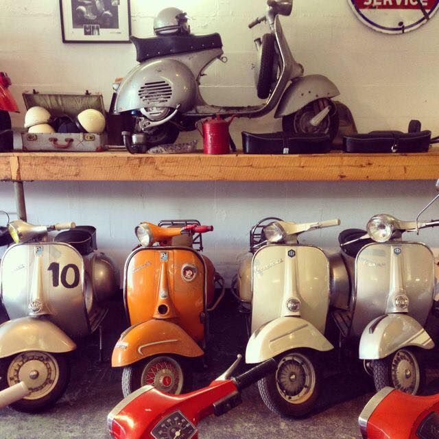 Multiple vintage Vespa scooters arranged on wooden shelves in an indoor display