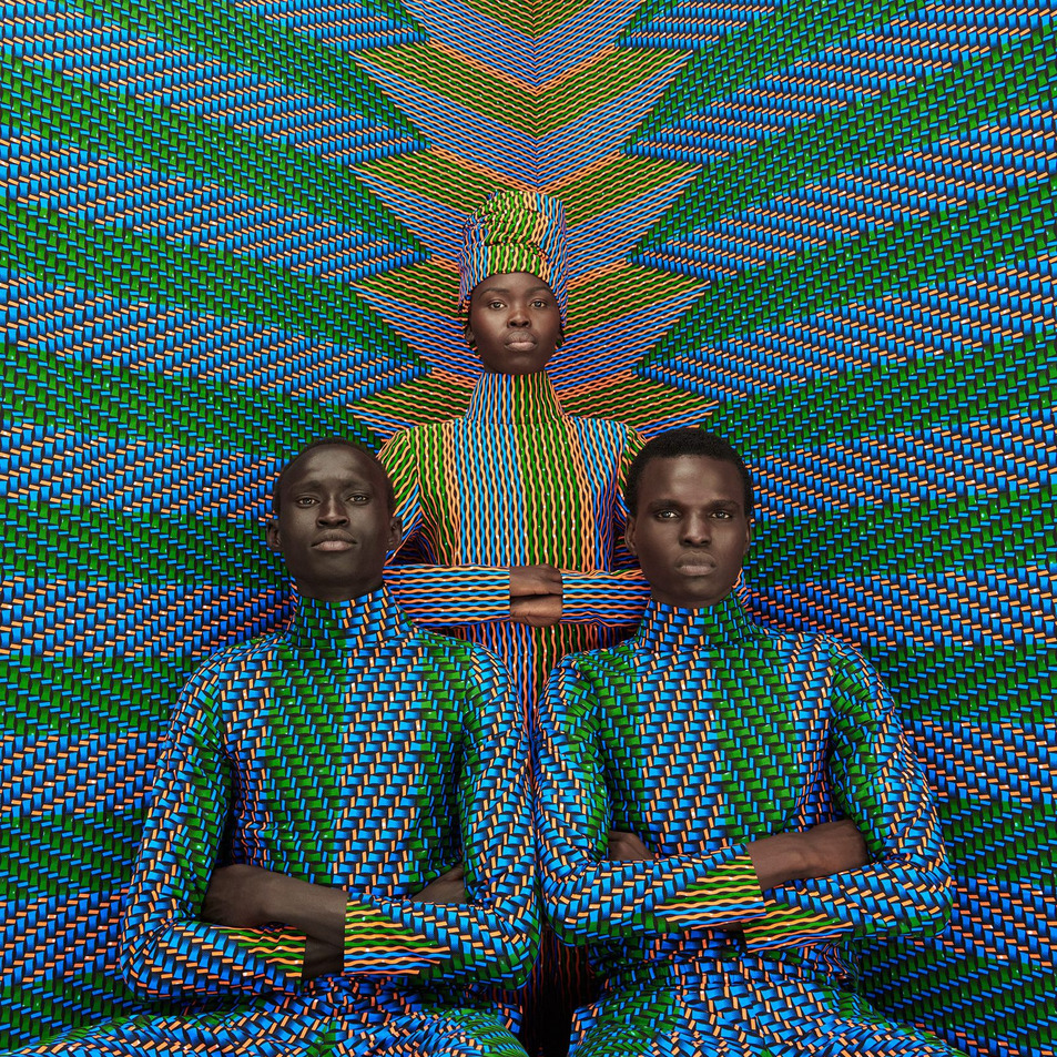 Three women in matching geometric patterned outfits posed against a colorful optical illusion background