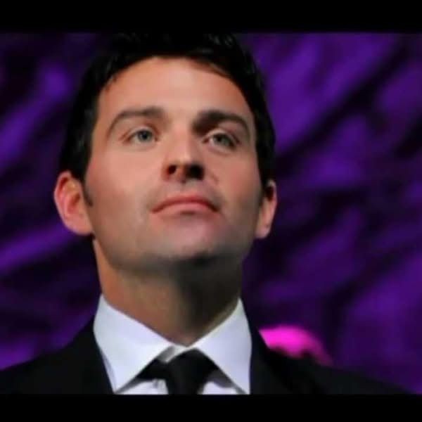 Portrait of man in black tuxedo and bow tie looking upward against purple background
