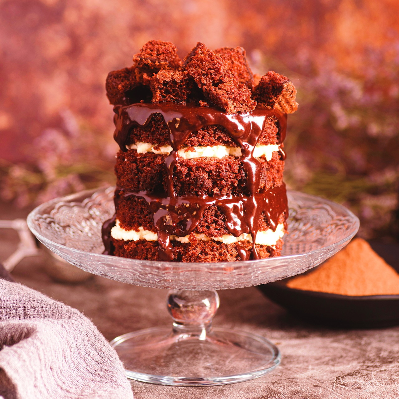 Slice of chocolate layer cake with cream filling and chocolate drizzle on a glass stand