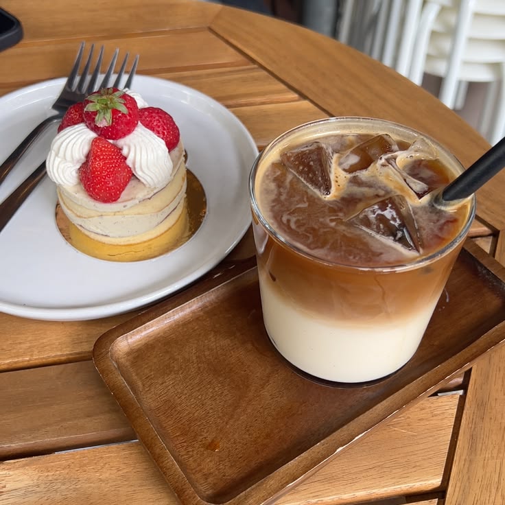 Iced coffee in a glass next to a strawberry cream cake on a wooden cafe table