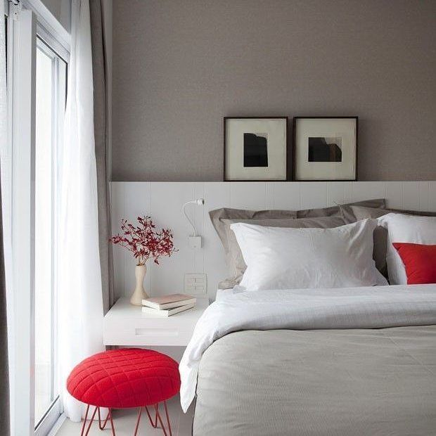 Modern bedroom with white bedding, gray walls, framed pictures, and a red stool near a window