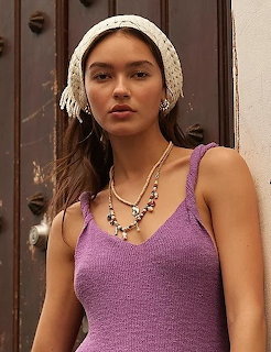 Young woman in purple knit tank top with beaded necklace and white lace headband near wooden door