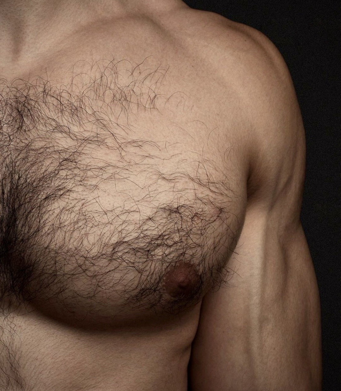 Close-up of a muscular shirtless male torso with chest hair on dark background