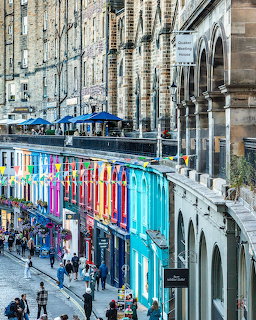 Colorful storefronts on Edinburgh's Victoria Street beneath historic stone buildings