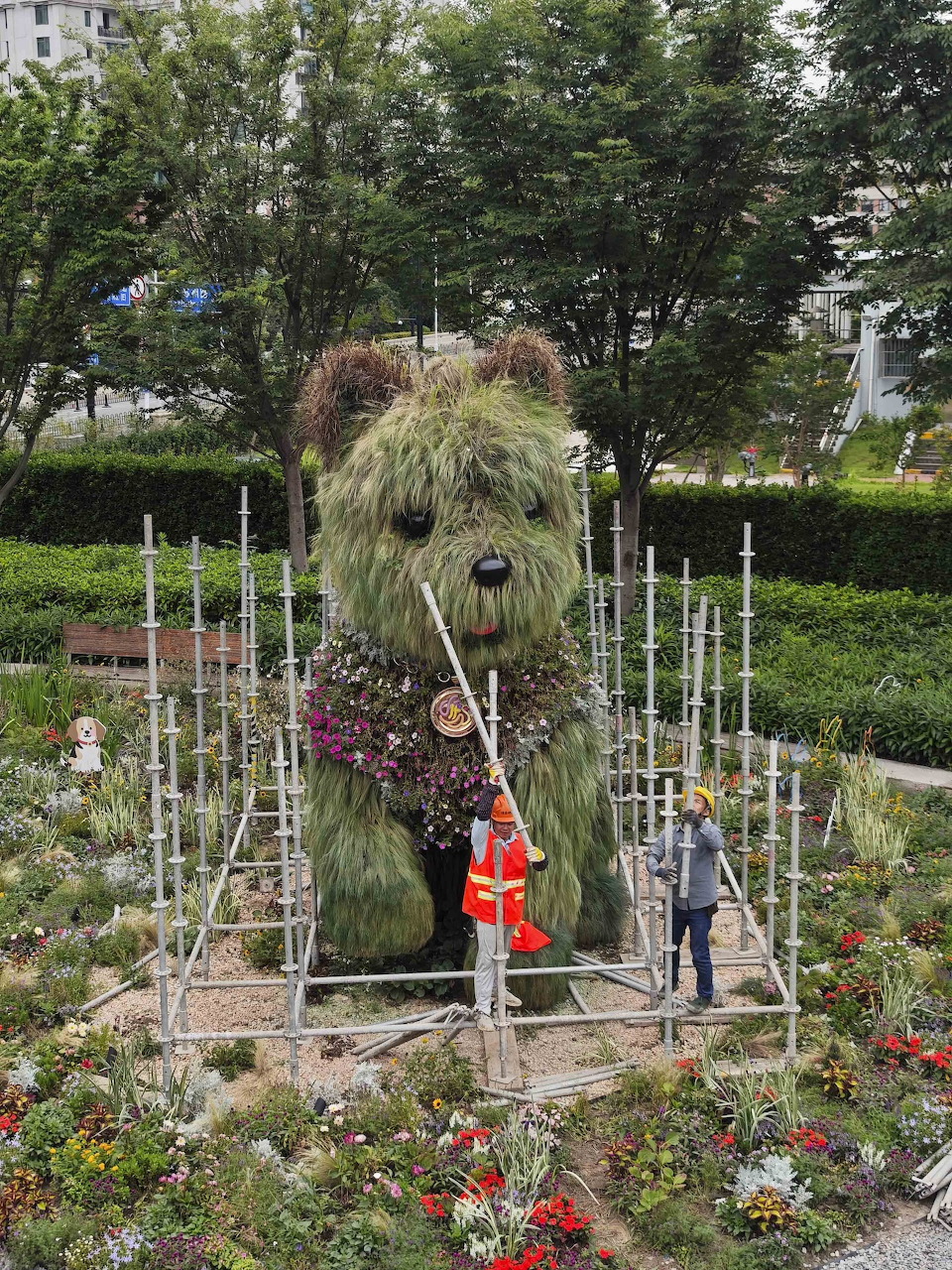 Large flower-covered dog topiary in a garden with two people standing beside it