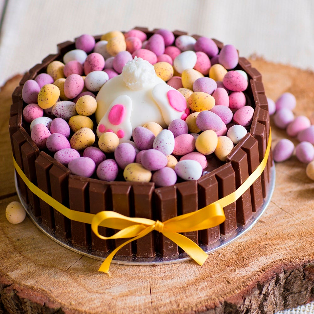 Chocolate cake with pastel candy eggs and a white bunny topper on a wooden slab