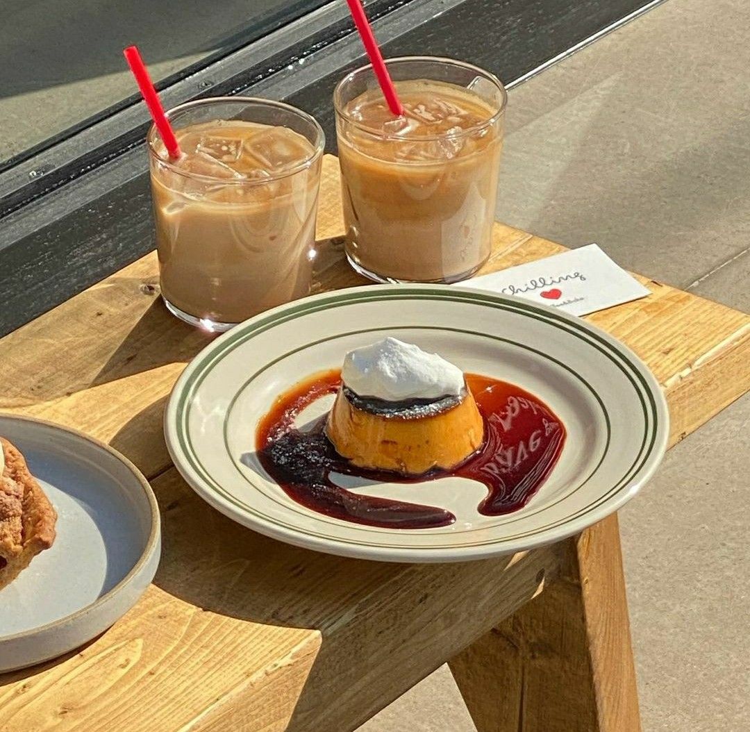 Two iced coffees and flan dessert with caramel and berry sauce on wooden table