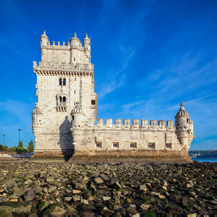 Belem Tower, a historic white stone fortress in Lisbon, standing by the water under a blue sky