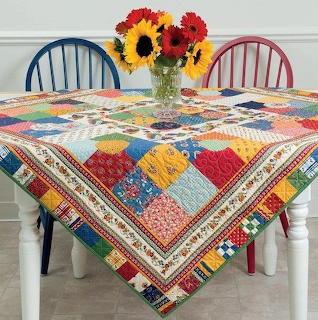 Colorful patchwork quilt on white table with flower vase centerpiece and two chairs