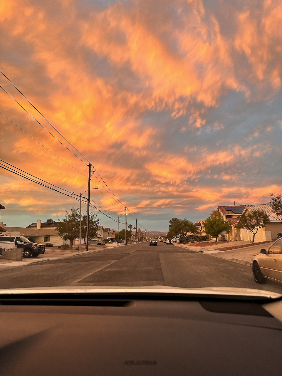 Dramatic orange sunset clouds over a suburban residential street with power lines and parked cars