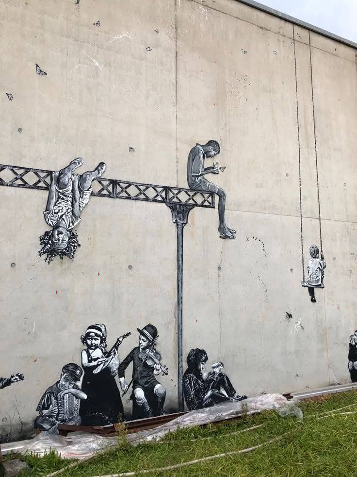 Black stencil street art figures painted on a tall concrete wall above grass