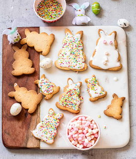 Overhead view of Easter cookies with icing, sprinkles, marshmallows, and decorative eggs on a board