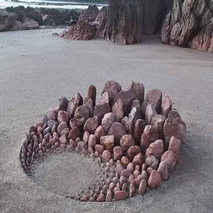 Spiral pattern made of stacked stones on beach sand with ocean cliffs