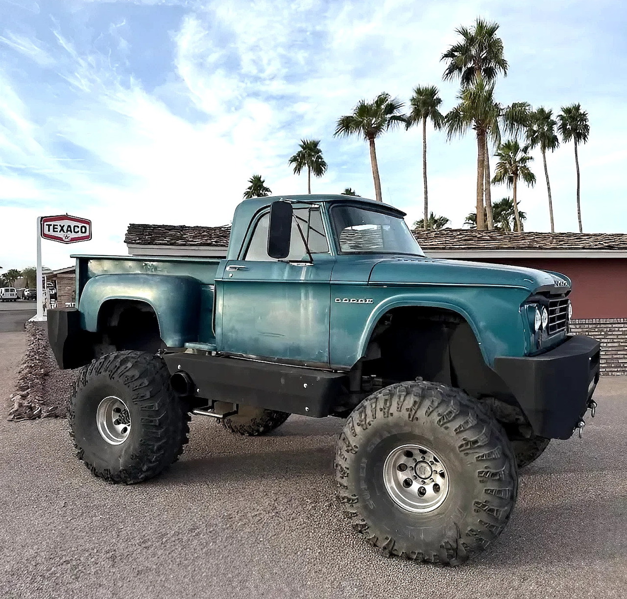 Turquoise 1962 Dodge D150 pickup truck with lifted suspension and oversized tires parked near palm trees