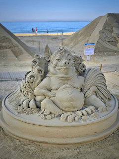 Intricate sand sculpture of a mythical dragon creature on a beach with ocean in background