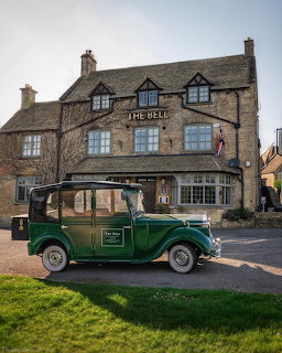 Green vintage car parked outside a stone inn building