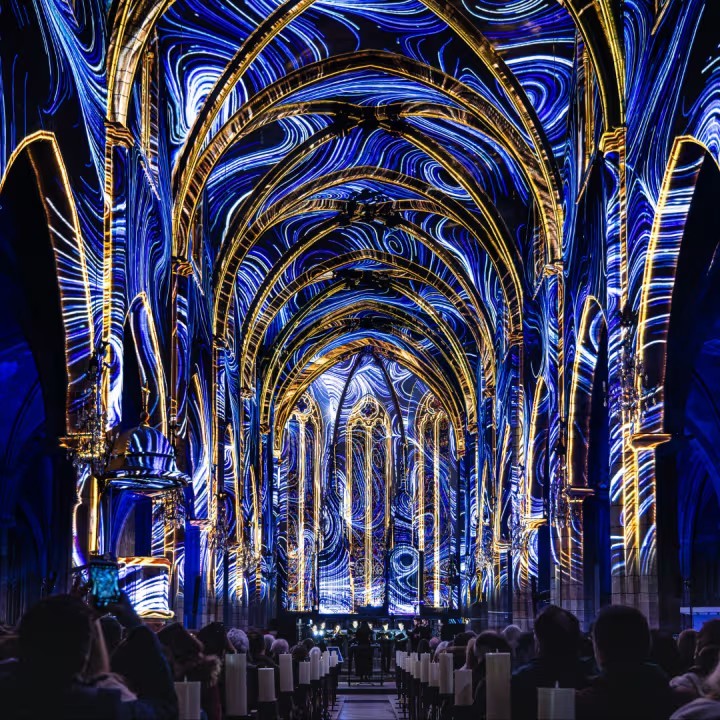 Blue and gold illuminated Gothic church interior with vaulted arches and people seated below