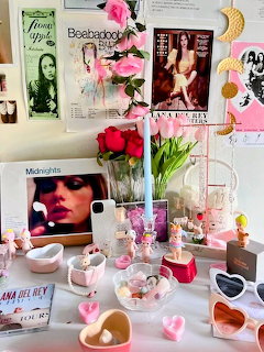 Coquette-style vanity with posters, pink flowers, candles, and heart-shaped decor on a white desk