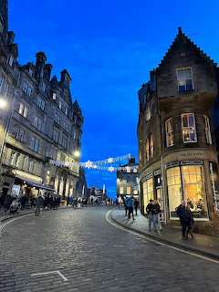 Curved cobblestone street in an old city at dusk with historic buildings, pedestrians, and lit windows