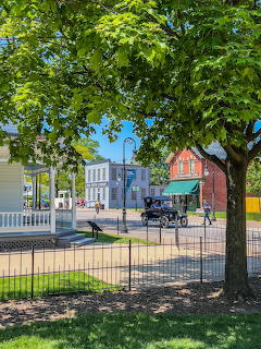 Sunny village scene with green trees, horse-drawn cariage, and historic buildings at Greenfield Village