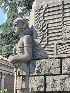 Stone winged sphinx statue with Egyptian headdress on an architectural wall with carved geometric patterns