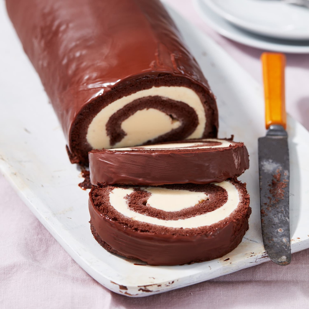 Sliced chocolate roll cake with white cream filling displayed on white platter