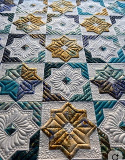Close-up of a star pattern quilt with teal, gold, and white geometric blocks and detailed quilting stitches