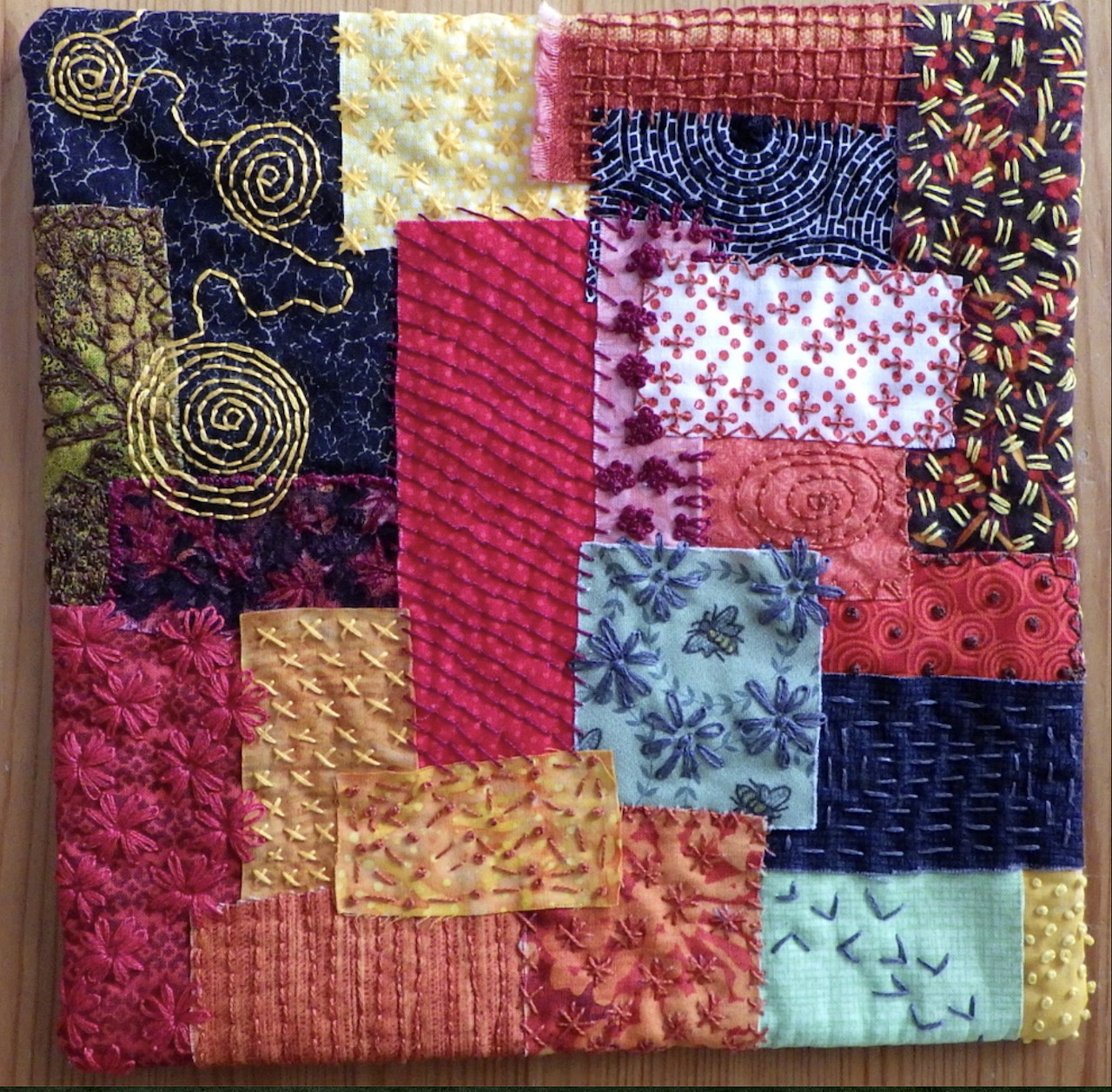 Colorful patchwork quilt with varied fabric squares featuring embroidery, polka dots, and textured stitching