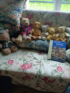 Several teddy bears on a floral sofa next to a teddy bear book