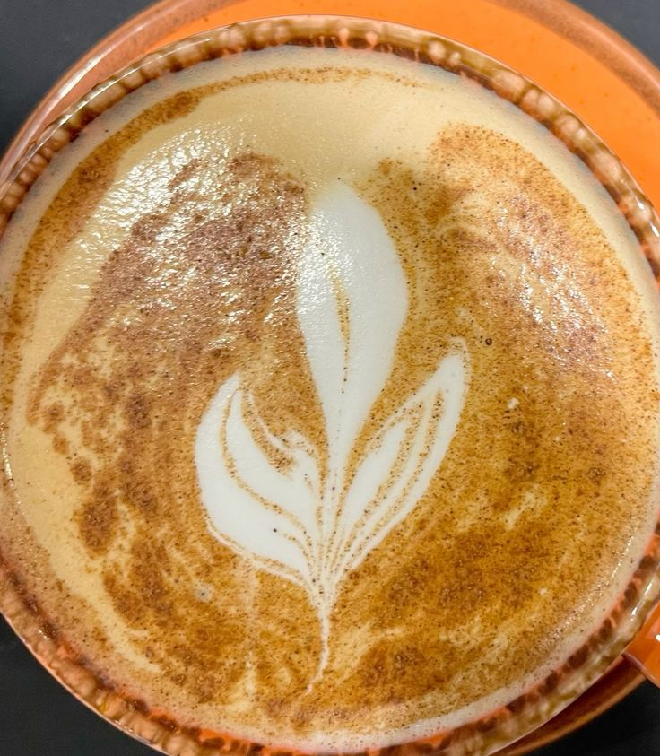 Coffee cup with decorative leaf latte art pattern dusted with cinnamon powder, viewed from above