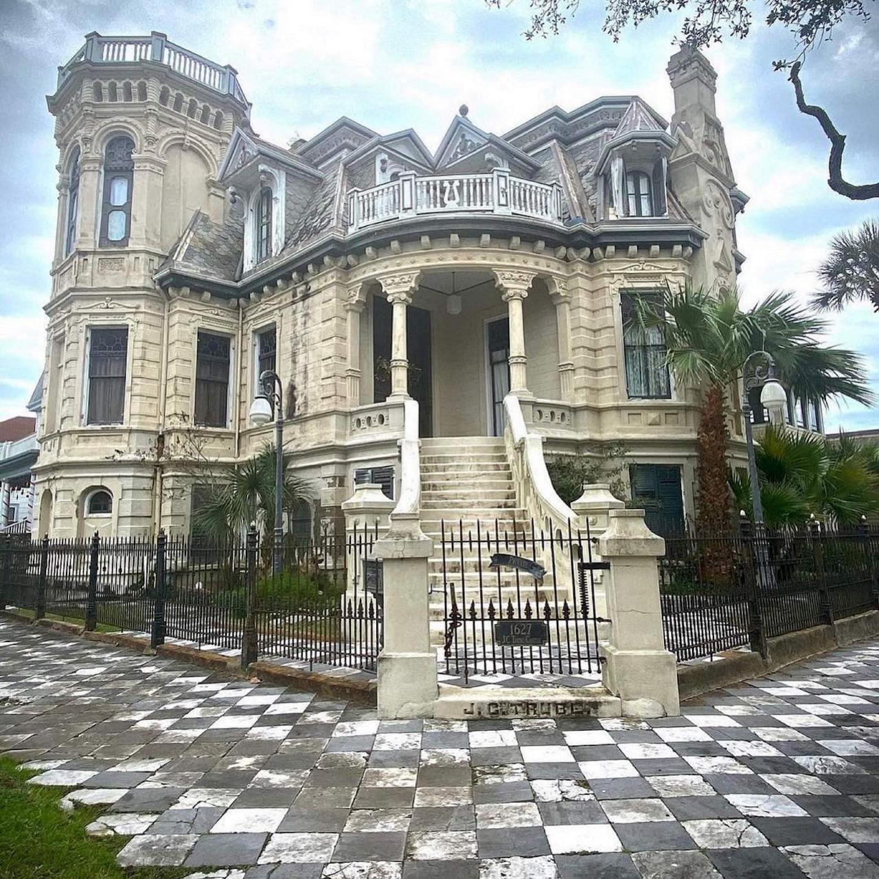 Grand Victorian stone mansion with turret, columns, palm trees, and black-white checkered courtyard